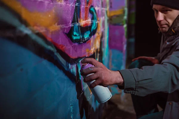Hombre pintando graffiti con pintura en aerosol en la pared por la noche - foto de stock