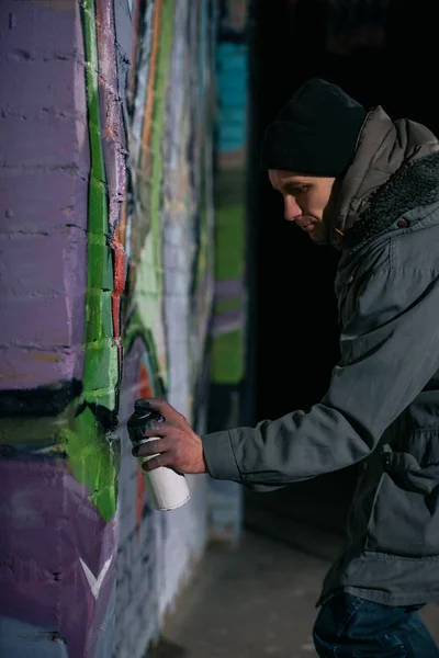 Artista callejero pintando graffiti con pintura en aerosol en la pared por la noche - foto de stock