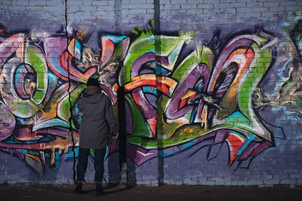 Back view of street artist painting colorful graffiti on wall at night — Stock Photo