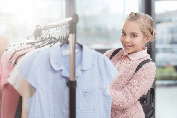 Niño sonriente elegir ropa en percha en la tienda - foto de stock