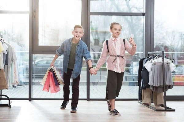 Niños felices con bolsas de compras haciendo selfie en la tienda - foto de stock