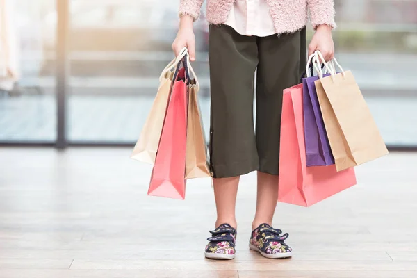 Abgeschnittenes Bild eines Kindes, das im Geschäft bunte Papiertüten hält — Stockfoto