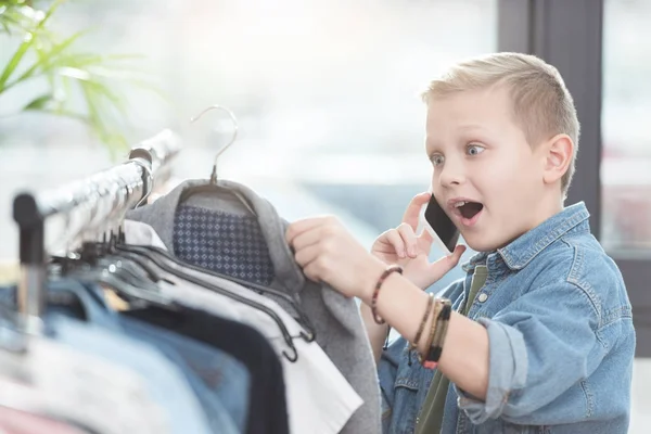 Garçon surpris en utilisant smartphone tout en tenant le tissu dans la main à la boutique — Photo de stock