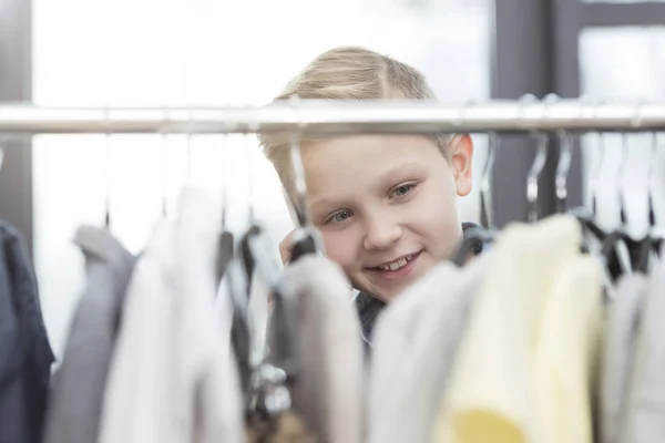Sonriente caucásico chico buscando en ropa en tienda - foto de stock