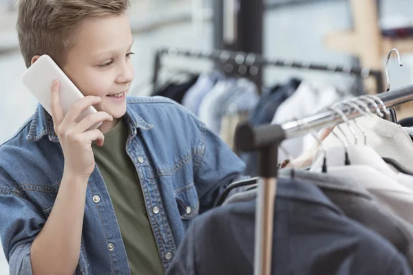 Garçon souriant à l'aide d'un smartphone tout en tenant le tissu dans la main à la boutique — Photo de stock