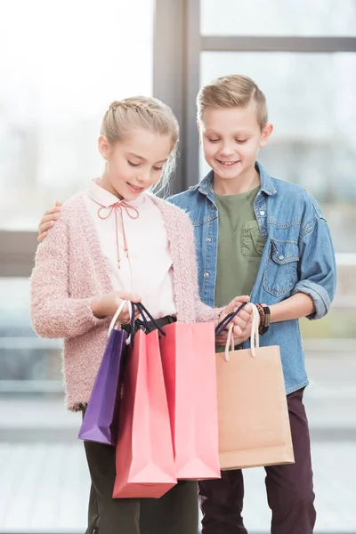 Due bambini felici che guardano giù su sacchetti di carta a negozio — Foto stock