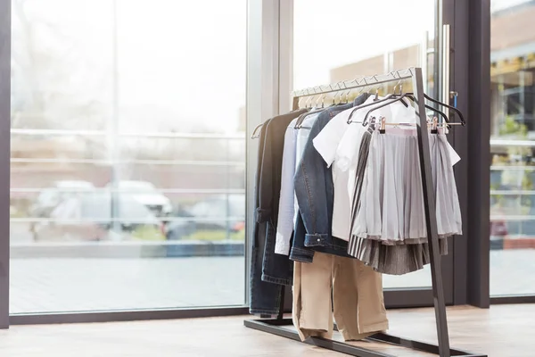 Varias ropas en hager en el interior de la tienda contra ventana - foto de stock