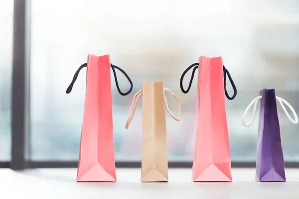 Colored paper bags laying in a row on surface against window — Stock Photo