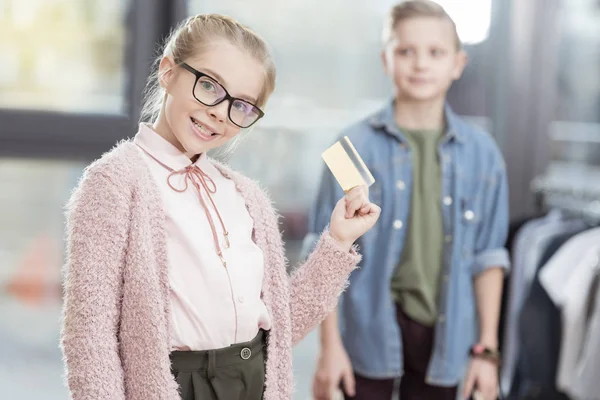 Smiling kid in glasses holding credit card with boy on blurred background — Stock Photo