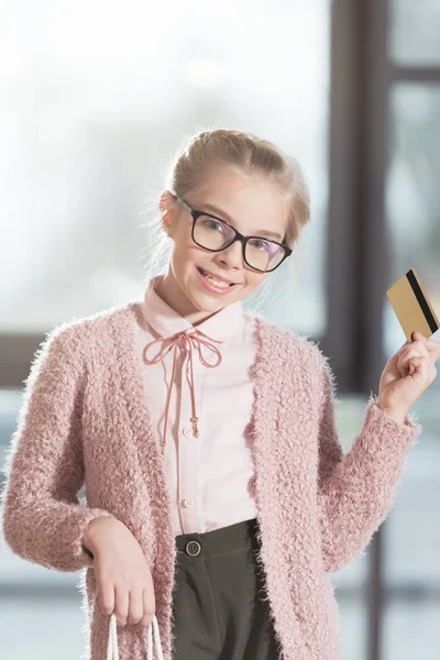 Enfant souriant dans des lunettes tenant la carte de crédit à l'intérieur de la boutique — Photo de stock