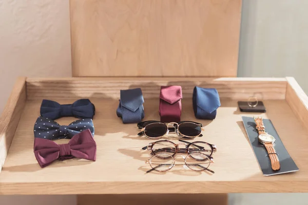 Papillon, cravatte, occhiali e orologio da polso in esposizione in legno presso il negozio — Foto stock
