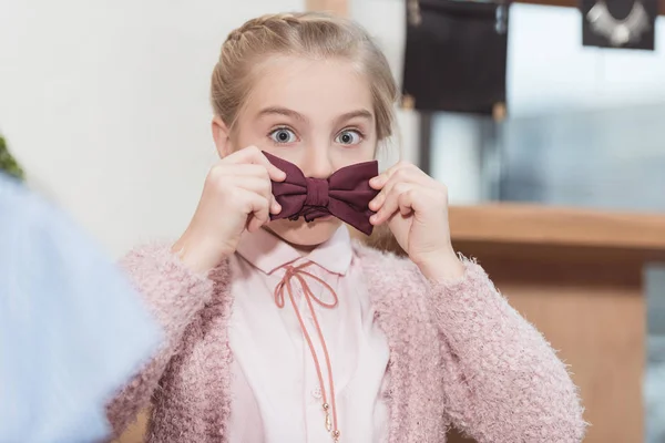 Feliz niña jugando con pajarita en las manos contra la boca - foto de stock