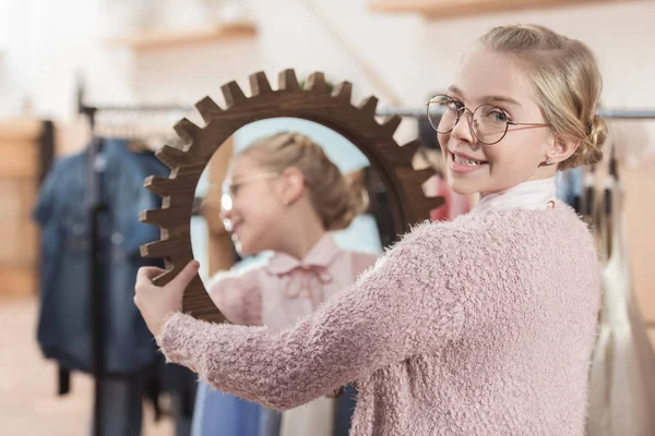 Счастливая девочка смотрит в камеру с зеркалом в руках в интерьере магазина — стоковое фото