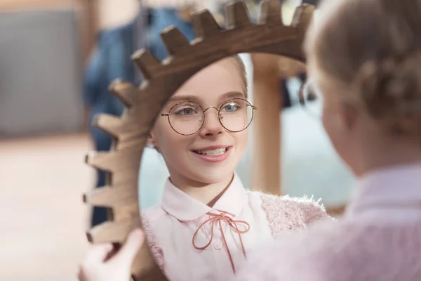 Улыбающийся ребенок смотрит в зеркало в руках в интерьере магазина — стоковое фото