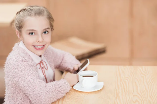 Bambino sorridente seduto a tavola con smartphone in mano — Foto stock