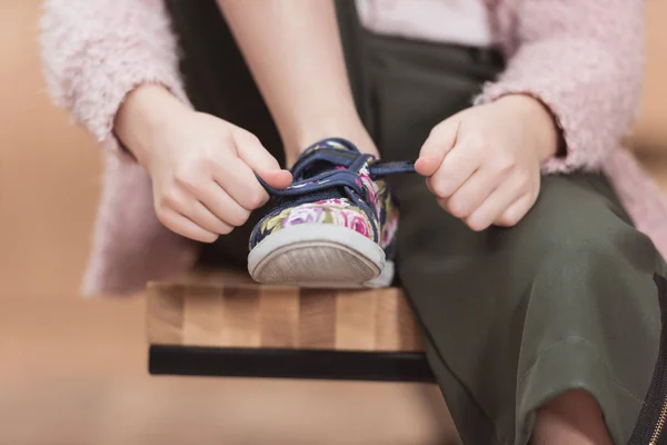Обрізане зображення дитини, що зв'язує мереживо на кросівки, сидячи — стокове фото