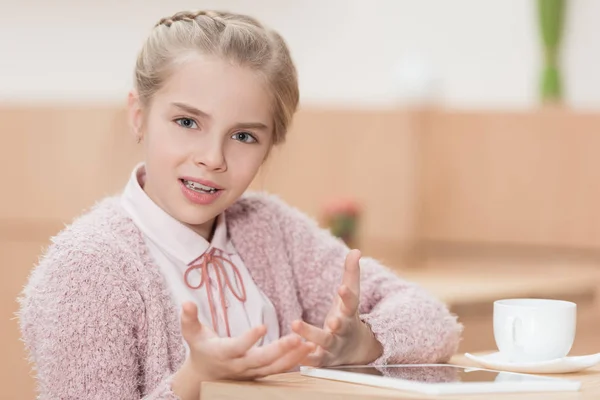 Kind sitzt mit digitalem Tablet am Tisch und blickt in Kamera — Stockfoto