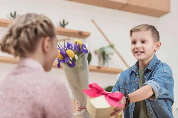 Smiling boy presenting bouquet and box with ribbon to girlfriend at cafe — Stock Photo