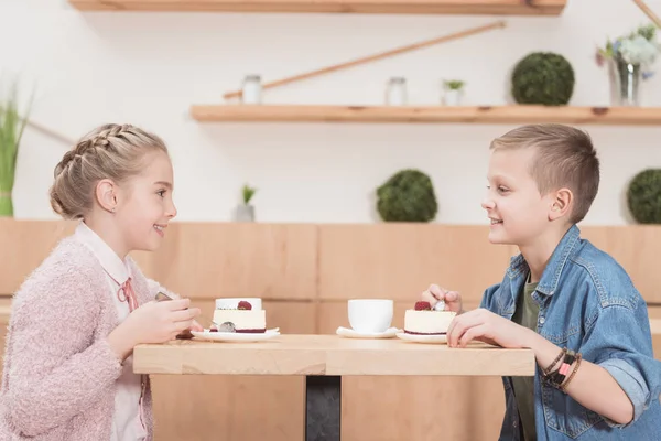 Children sitting at table at cafe while looking at each other and smiling — Stock Photo
