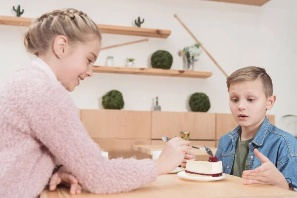 Crianças sentadas à mesa no café enquanto olham para o bolo na mesa no café — Fotografia de Stock