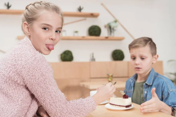 Дитина показує язик на камеру, сидячи за столом проти хлопчика в кафе — стокове фото