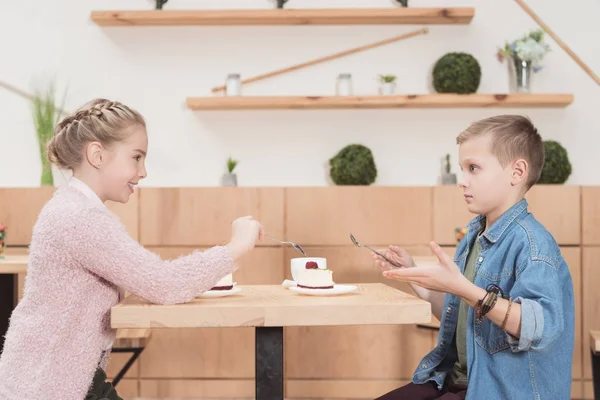Niños sentados en la mesa en la cafetería mientras se miran - foto de stock