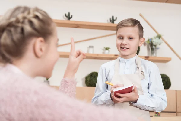 Piccolo cameriere prendere appunti in blocco note contro il bambino con indice sollevato al caffè — Foto stock