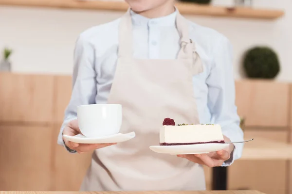 Середина хлопчика в дитині тримає чашку і десерт в руках в кафе — стокове фото