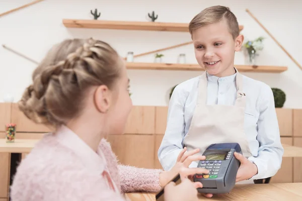 Niño pagando con tarjeta de crédito con terminal en la cafetería - foto de stock