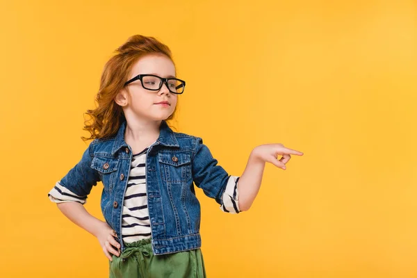 Portrait of cute little kid in eyeglasses pointing away isolated on yellow — Stock Photo