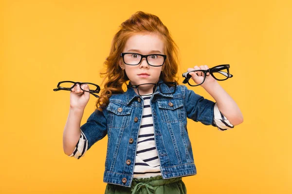 Portrait of shocked child showing eyeglasses in hands isolated on yellow — Stock Photo
