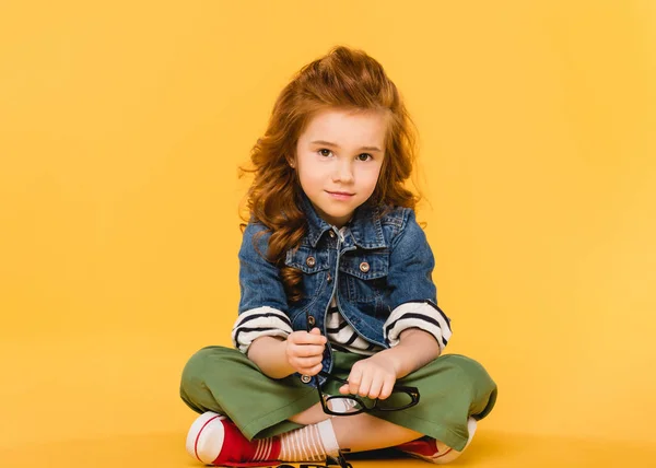 Smiling child with eyeglasses in hands looking at camera isolated on yellow — Stock Photo