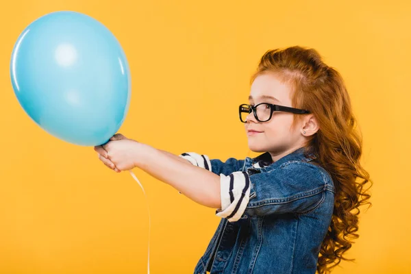 Side view of kid in eyeglasses with balloon in hands isolated on yellow — Stock Photo