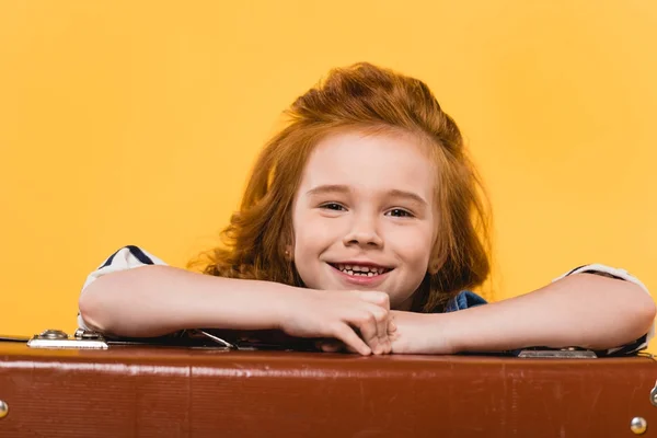 Retrato de un niño sonriente apoyado en una maleta aislada en amarillo - foto de stock