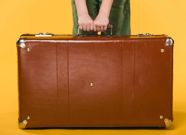 Partial view of child holding leather suitcase isolated on yellow — Stock Photo