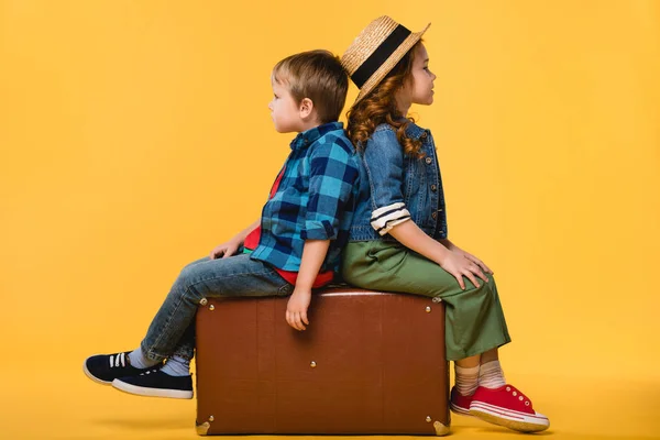 Vista laterale dei bambini seduti su una valigia di pelle isolata sul giallo — Foto stock