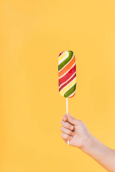 Partial view of kid holding lollipop in hand isolated on yellow — Stock Photo