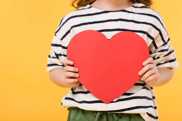 Vista parcial de niño con corazón de papel rojo en manos aisladas en amarillo, San Valentín concepto de día - foto de stock