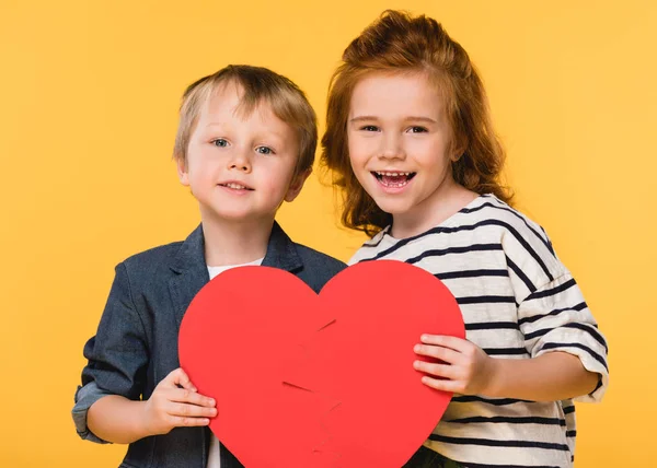 Retrato de niños sosteniendo el corazón de papel rojo juntos aislados en el concepto de día de San Valentín amarillo - foto de stock