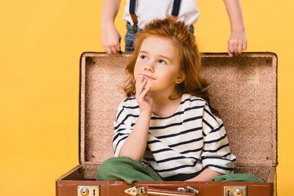 Vista parziale del bambino sognante seduto in valigia con ragazzo in piedi vicino isolato sul giallo — Foto stock