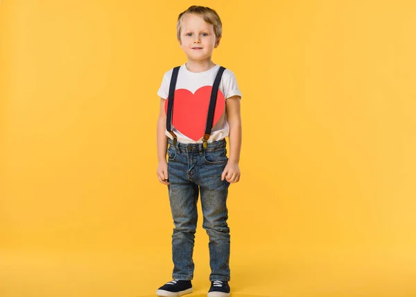 Adorable little boy with red paper heart isolated on yellow, st valentines day concept — Stock Photo