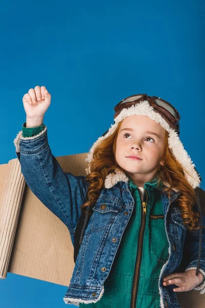 Portrait of adorable preteen kid in pilot costume with paper plane wings isolated on blue — Stock Photo