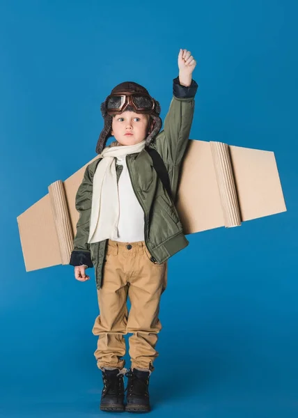 Милый маленький мальчик в костюме пилота с крылом бумажного самолета, изолированным на голубом — стоковое фото