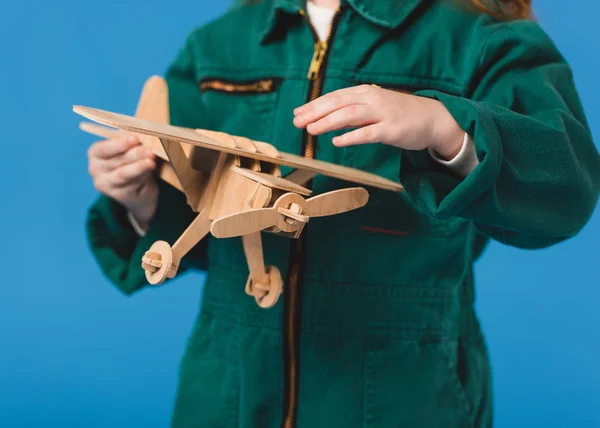 Tiro cortado de criança em traje piloto com brinquedo de avião de madeira isolado em azul — Fotografia de Stock