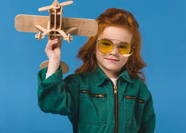 Retrato de niño sonriente en traje de piloto con juguete plano de madera aislado en azul - foto de stock