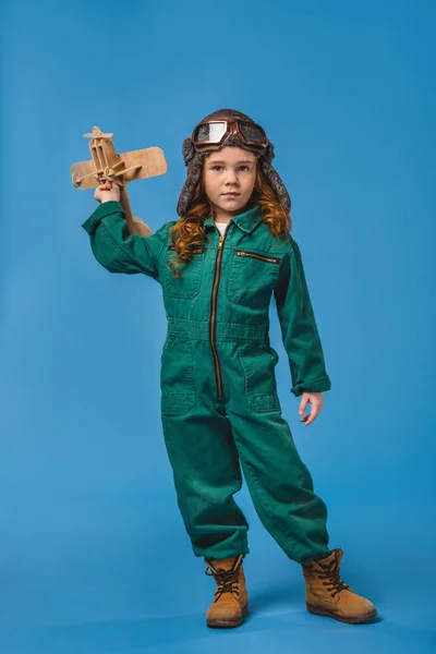 Adorabile bambino in costume da pilota con giocattolo aereo in legno isolato su blu — Foto stock