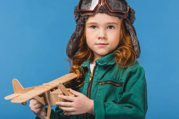 Portrait of adorable child in pilot costume with wooden plane toy isolated on blue — Stock Photo