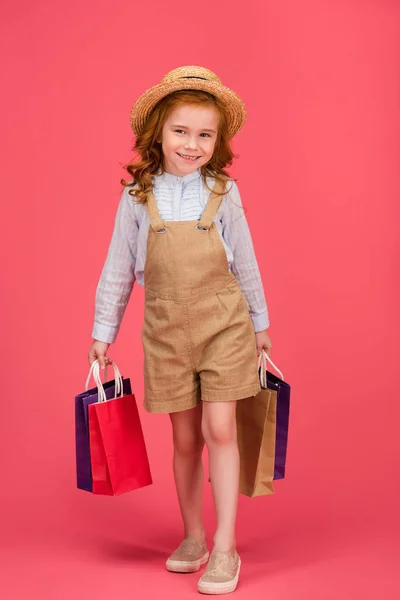 Niño sonriente en ropa casual con bolsas de compras aisladas en rosa - foto de stock