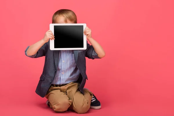 Kleiner Junge verdeckt Gesicht mit Tablet mit leerem Bildschirm isoliert auf rosa — Stockfoto