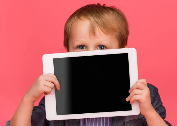 Pequeño niño cubriendo la cara con la tableta con la pantalla en blanco aislado en rosa - foto de stock